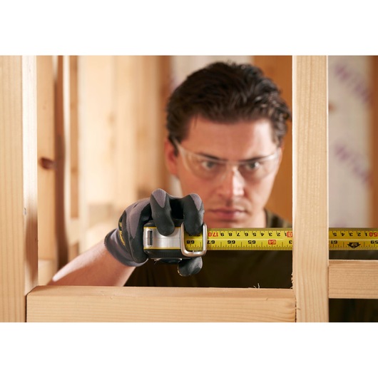 STANLEY FMHT38215-5 tape measure in use for wood framing, close-up view of yellow tape in gloved hand.