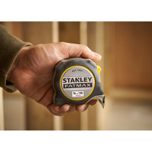 STANLEY FMHT38215-5 FatMax tape measure held in hand, grey and yellow casing, close-up.
