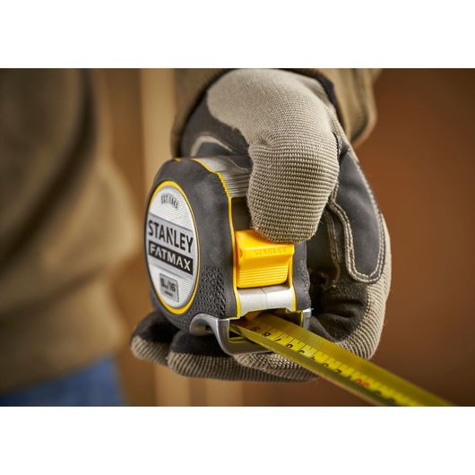 STANLEY FMHT38215-5 tape measure held by gloved hand, close-up, product photography.