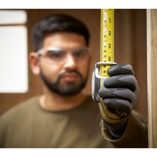STANLEY FMHT38215-5 tape measure held vertically by gloved hand during construction.