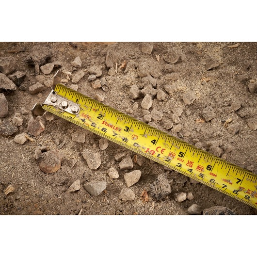 STANLEY FMHT38215-5 yellow tape measure on dirt and rocks, close-up photo.