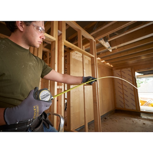 Photo of STANLEY FMHT38218-5 tape measure extended by gloved hand on construction site framework.