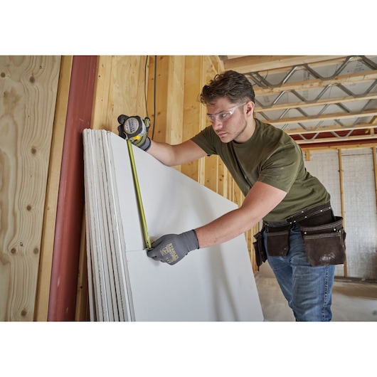 STANLEY FMHT38218-5 tape measure used by worker measuring drywall in construction photography.