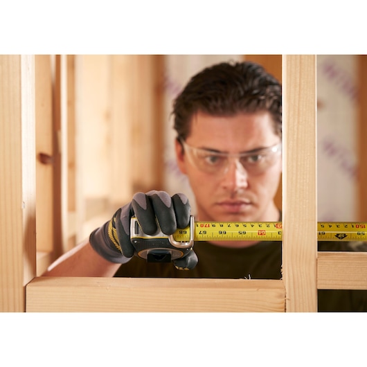 STANLEY FMHT38218-5 tape measure held by gloved hand in construction framing context.