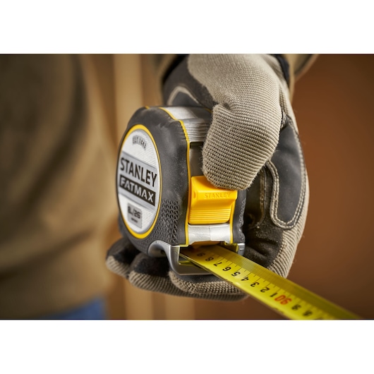 Photo of STANLEY FMHT38218-5 FATMAX tape measure held in gloved hand, yellow blade extended.