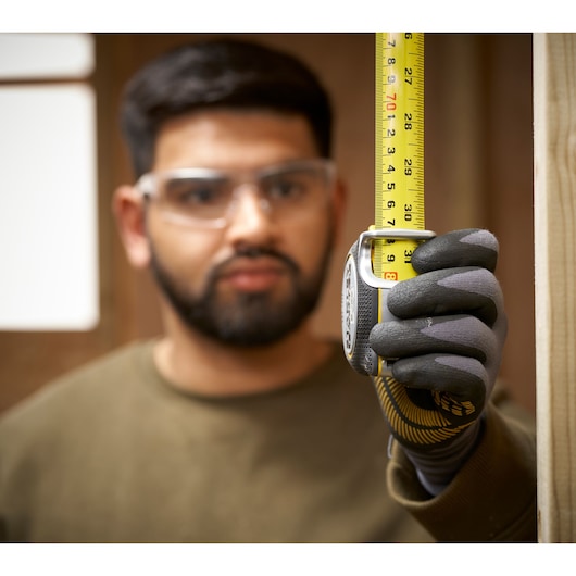 Stanley FMHT38218-5 tape measure held vertically by gloved hand during measurement, close-up photography.