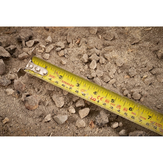 STANLEY FMHT38218-5 yellow tape measure on rocky soil, photography close-up of measurement tool.
