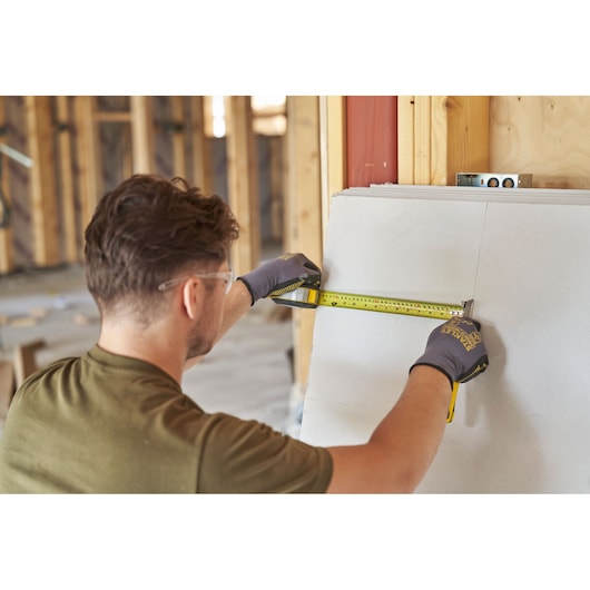 Photo of worker using STANLEY FMHT38218-5 tape measure on drywall at construction site.