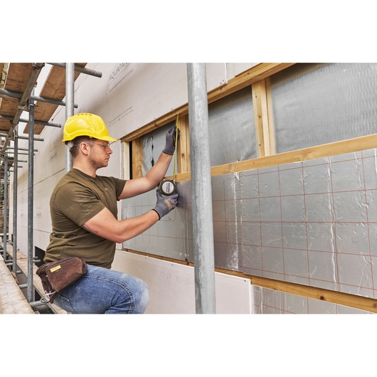 STANLEY FMHT38233-5 tape measure used by worker on construction site exterior wall, side angle.