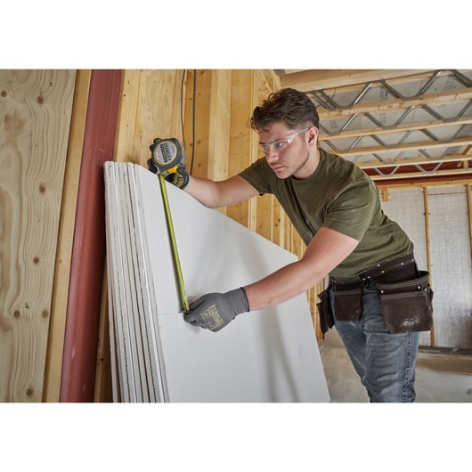 Photo of worker using STANLEY FMHT38233-5 tape measure to measure drywall sheets in a construction site.