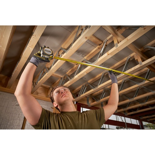 STANLEY FMHT38233-5 tape measure used by a person measuring wooden beams in a construction setting.