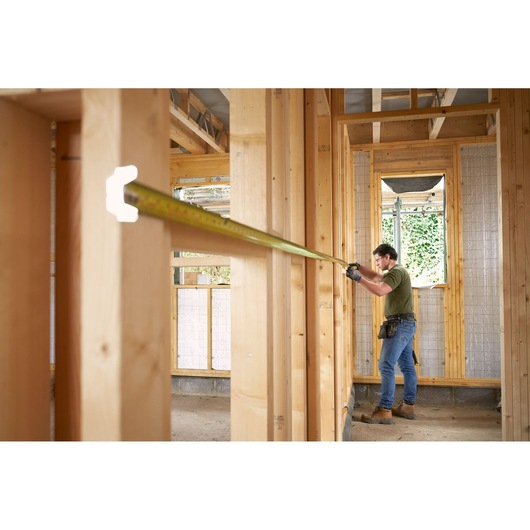 STANLEY FMHT38233-5 tape measure in use on a construction site, worker measuring wooden wall framing.