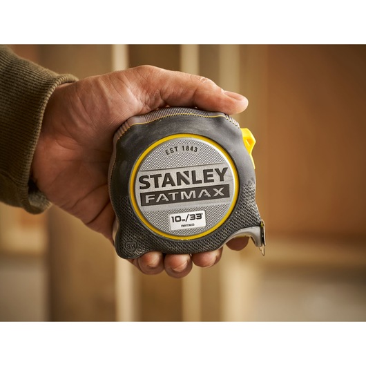 Photo of STANLEY FMHT38233-5 FatMax tape measure held in hand, black and yellow, close-up view.