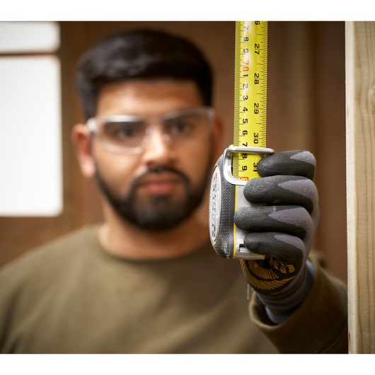 STANLEY FMHT38233-5 tape measure held vertically by gloved hand during measurement in construction setting.