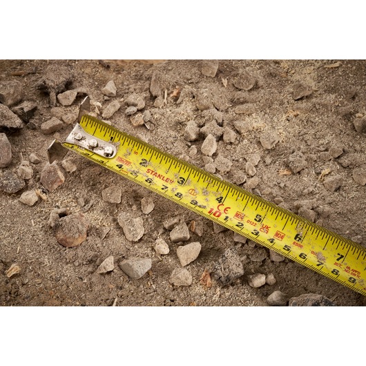 STANLEY FMHT38233-5 tape measure on rocky dirt surface, close-up showing yellow blade and markings.