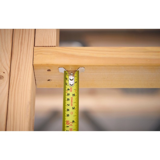 Stanley FMHT38233-5 tape measure measuring wood beam, close-up photo.
