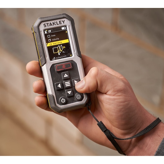 Photo of STANLEY FMHT77050-XJ laser distance meter held in hand, showing screen and control buttons.