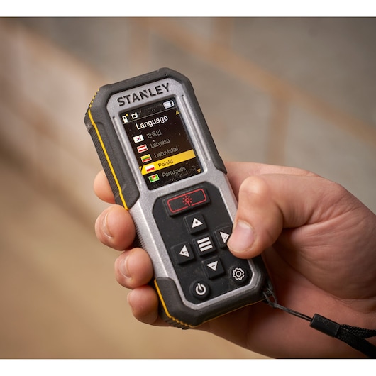 Stanley FMHT77050-XJ laser distance measurer, close-up in hand with screen showing language selection.