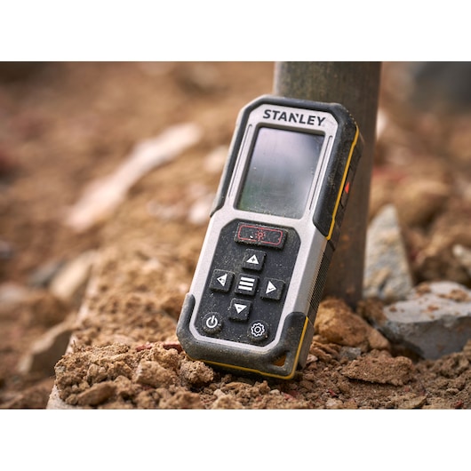 STANLEY FMHT77050-XJ laser distance measurer in rugged outdoor setting, close-up view.