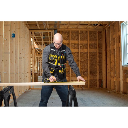 STANLEY FMST1-71181 tool vest with multiple yellow and black pockets, worn by a person working in a wood construction site.