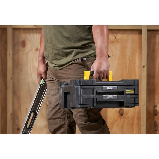 Photo of STANLEY FMST1-71969 tool box with yellow handle, carried by person, shown from the side indoors.