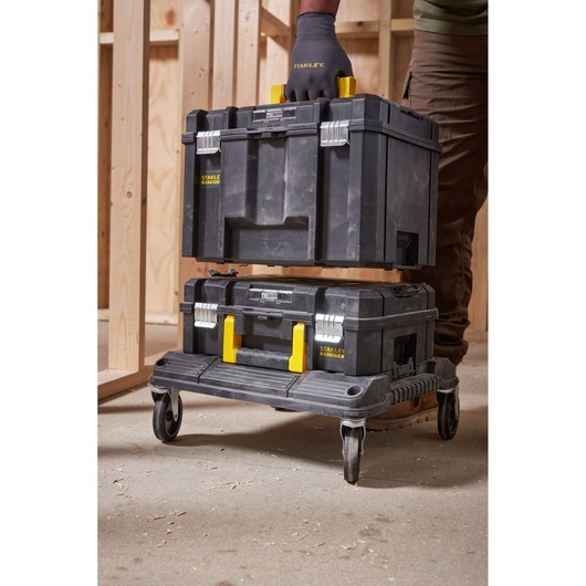 Stanley FMST1-71971 black tool box with yellow handle, side angle photo in workshop on wheeled platform.