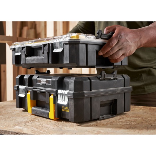 STANLEY FMST82967-1 stackable black toolboxes with yellow latches, person handling upper unit, side angle.