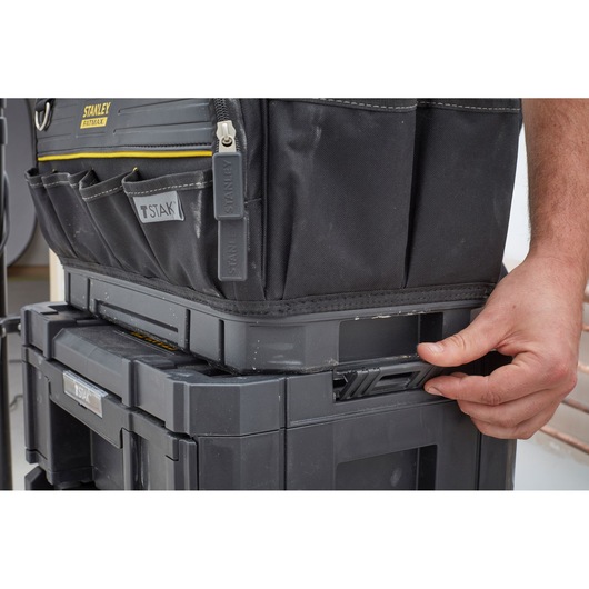STANLEY FMST83296-1 black tool bag on TSTAK storage box, close-up side angle, hand unlocking latch.