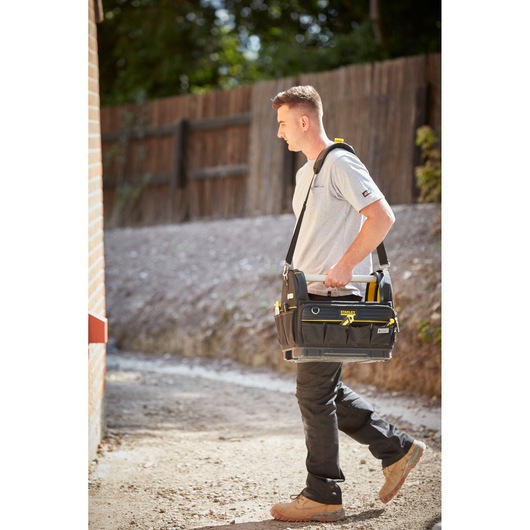 STANLEY FMST83296-1 black tool bag with yellow accents, carried over shoulder by worker outdoors.