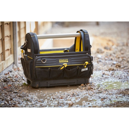 STANLEY FMST83296-1 tool bag with handle and pockets, black and yellow, on wet construction ground.