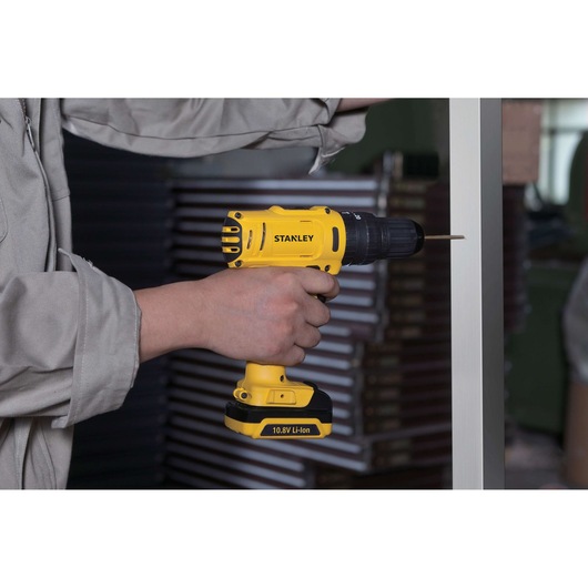 Stanley SCH12S2 cordless drill, yellow with black accents, used to drill metal surface.