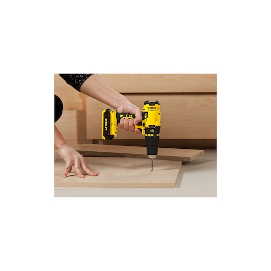 STANLEY SCH201D2K cordless drill in use, yellow and black, drilling on wooden board indoors.