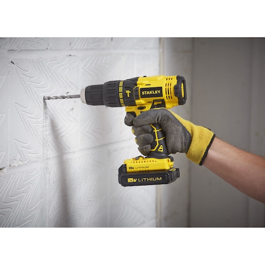 STANLEY SCH20S2K cordless drill in use on a white wall, close-up showing 18V Lithium battery.