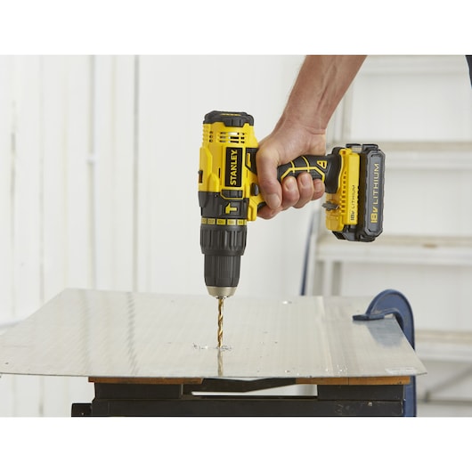 Photo of STANLEY SCH20S2K cordless drill in hand drilling into a metal sheet, side angle view.