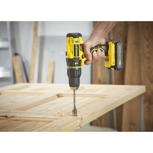 Stanley SCH20S2K cordless drill with 18V lithium battery drilling wood, close-up side view.