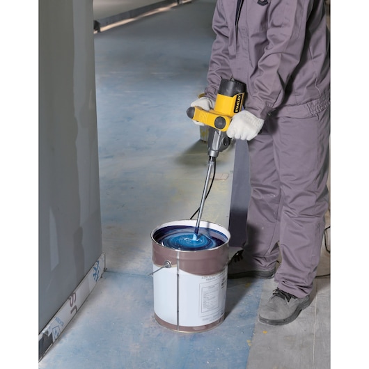 STANLEY SDR1400-KR electric mixer in use, mixing blue paint in a large bucket on a construction site floor.
