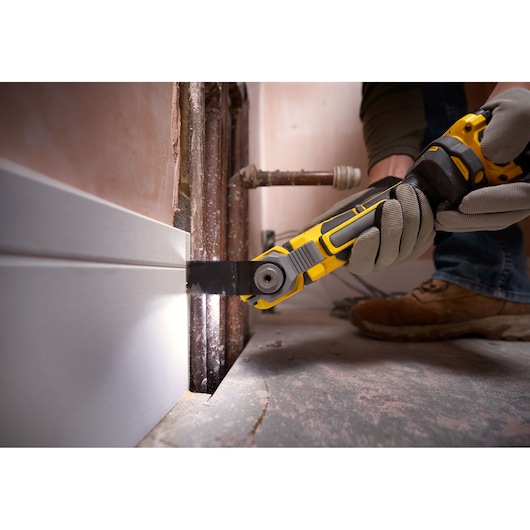 STANLEY SFMCE510B oscillating multi-tool cutting baseboard near pipes, handheld close-up during renovation.