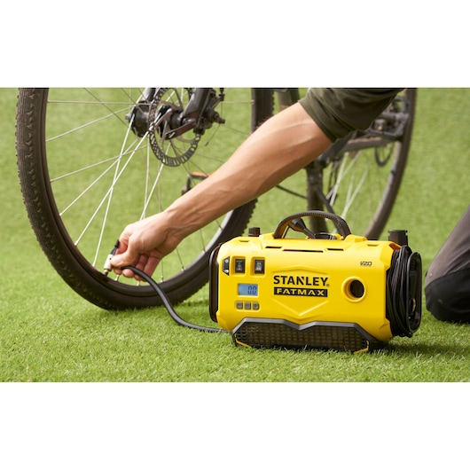 STANLEY SFMCE520B portable inflator in use, inflating a bicycle tire on green grass, front angle.