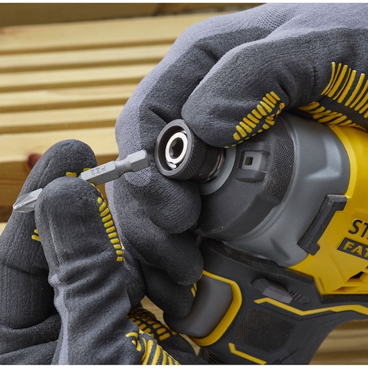 Photo of STANLEY SFMCF820B impact driver being fitted with a bit, close-up angle, gloved hands visible.