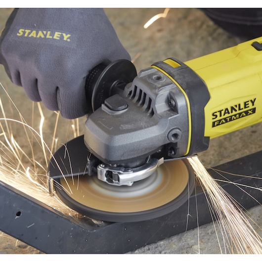Stanley SFMCG400D1K angle grinder in use, yellow body, cutting metal with sparks, close-up.