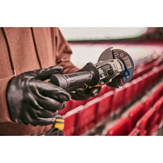 STANLEY SFMCG700M2K cordless angle grinder held by gloved hands in a stadium setting.