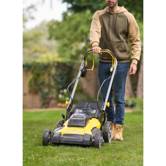 Photo of STANLEY SFMCMWS251B lawn mower in use outdoors, yellow and black design, front angle view.