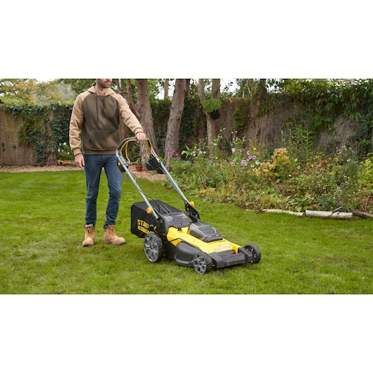 Photo of STANLEY SFMCMWS251B lawn mower with black and yellow body shown in a garden setting.