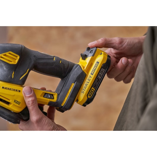 Photo of STANLEY SFMCW221B sander in use, close-up showing V20 battery and ergonomic yellow-black handle.