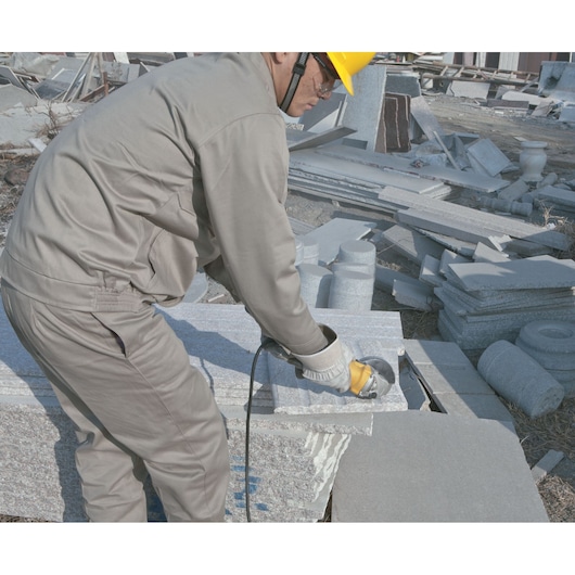 STANLEY SGS1045 angle grinder in use by worker cutting stone slab at construction site.