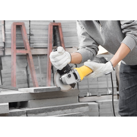 STANLEY SGV115 angle grinder with yellow handle in use cutting concrete block, close-up.