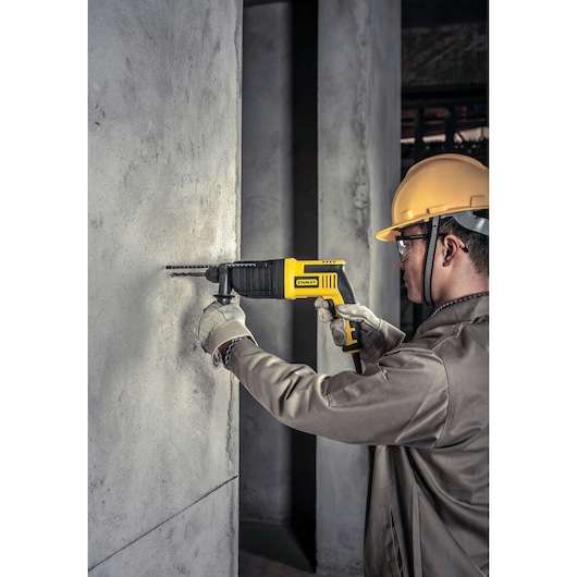 STANLEY SHR263KC rotary hammer drill in use drilling concrete wall, yellow and black design, product photography.