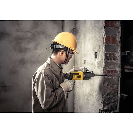 STANLEY SHR263KC rotary hammer drill in use, side angle, drilling into concrete wall, construction setting.