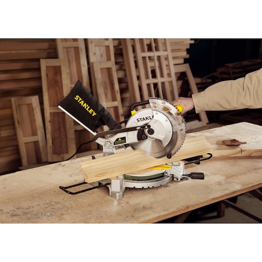 Photo of STANLEY SM16-B3 miter saw cutting wood on a workbench in a woodworking workshop.