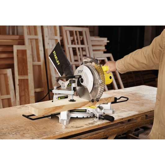 STANLEY SM16-B3 miter saw in use, cutting wooden plank, workshop background, photography angle from side.